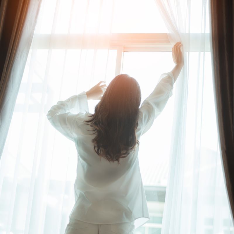 カーテンを開けて朝日を浴びる女性