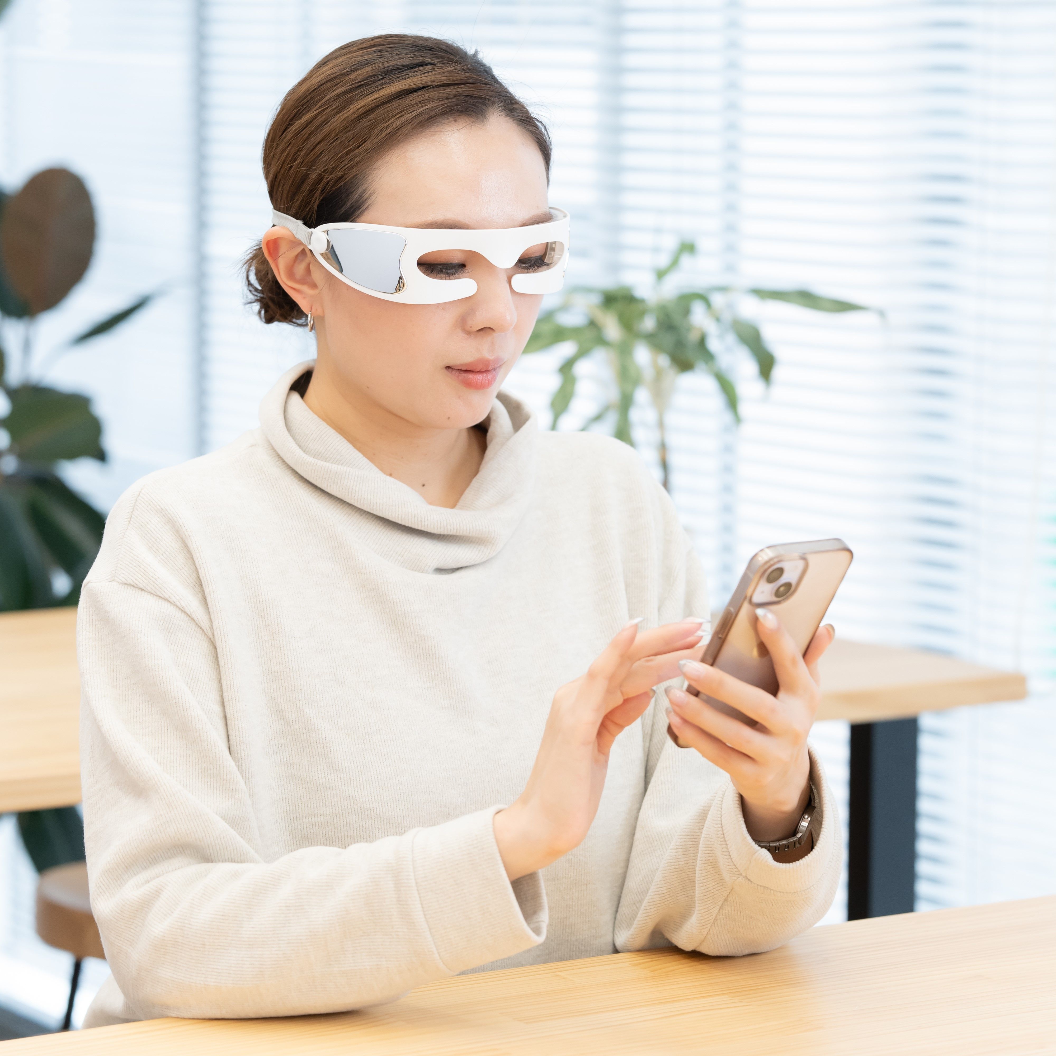 LEDアイマッサージャーをしながらスマホを見る女性