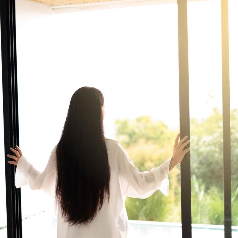 窓を開けて朝陽をあびる女性